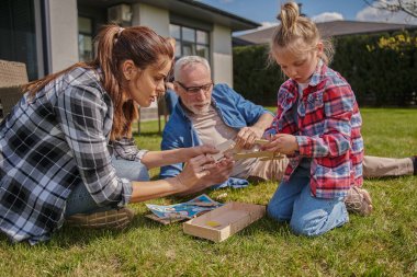 Yoğunlaşmış anne çimenlerde oturup kızıyla ve dışarıda olgun babasıyla oynuyor. Aile bağları kavramı