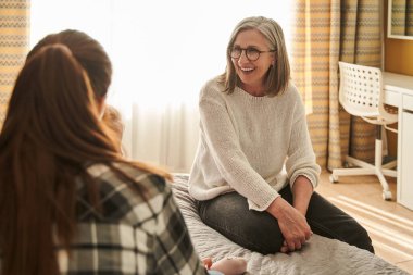 Mutlu olgun bir kadın rahat yatak odasında kızıyla konuşurken gülüyor. Aile bağları ve insan ilişkileri kavramı