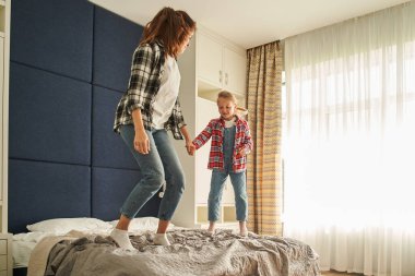 Şefkatli Kafkas anne ve kızı yatakta birlikte oynuyorlar. Mutlu anne ve çocuk yatakta zıplıyor, eğleniyor, yatak odasında eğlenceli anlar yaşıyor.