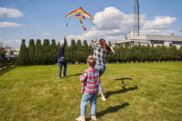 Overjoyed family of three playing with kite and having fun at the open air. Happy relationships concept. Stock photo