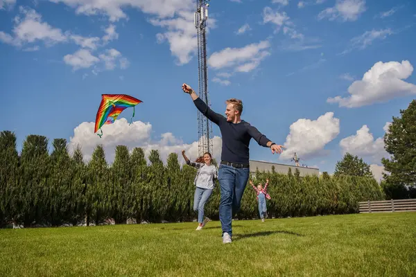 Overjoyed family of three playing with kite and having fun at the open air. Happy relationships concept. Stock photo