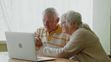 Kafkasyalı yaşlı çift ellerinde haplarla güneşli oturma odasında görüntülü görüşme yapıyorlar. Emeklilik, birliktelik, sağlık ve sağlık, tıp, kıdemli yaşam tarzı, iletişim, teknoloji, değiştirilmemiş