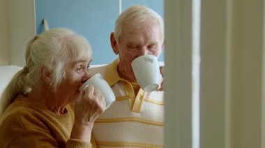 Mutlu son sınıf çifti sıcak içecekle kahve içerken ve evde birbirlerine gülümserken. Emeklilik yaşam tarzı ve mutlu evlilik kavramı