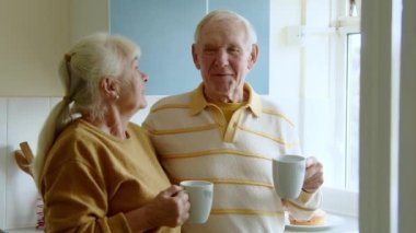 Mutlu, çekici, son sınıf çifti beyaz, rahat bir mutfakta durup, sabah kahvelerini yudumluyor, günaydın diyor ve günlük planlarını paylaşıyor.