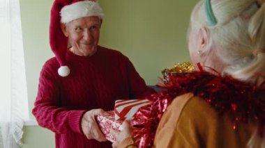 Güzel beyaz adam yeni yılı kutlarken karısına hediye sunar. Olgun emekliler için mutlu bir yaşam tarzı, parti ışıkları