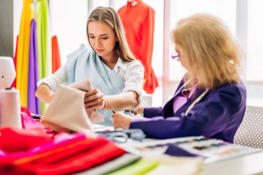 Genç ve güzel sahibinin portresi. Moda tasarımcısı. Moda tasarımı atölyesinde dikiş makinesi ve renkli kumaşlarla çalışan kıdemli kadın tasarımcı.