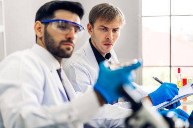 Profesyonel iki bilim adamı test tüpünde sıvı analiz ederken ve karıştırırken kimyasal bir deney yapıyor. Genç bilim adamı laboratuvarda cam üzerine kimyasal örnekler bırakıyor.