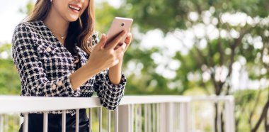 Gülümseyen mutlu Asyalı kadın portresi dijital akıllı telefon kullanarak rahatlıyor. Genç Asyalı kız ekranda yazı yazma ve şehirdeki sosyal medya oyunlarına bakıyor.