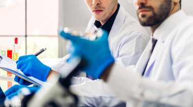 Profesyonel iki bilim adamı test tüpünde sıvı analiz ederken ve karıştırırken kimyasal bir deney yapıyor. Genç bilim adamı laboratuvarda cam üzerine kimyasal örnekler bırakıyor.