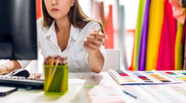 Genç ve güzel sahibinin portresi iş kadını moda tasarımcısı şık bir şekilde oturuyor ve çalışıyor. Genç tasarımcı kız, moda atölyesinde masa üstü ürünü ve renkli kumaşlar kullanıyor.