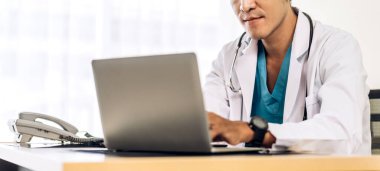 Steteskopla üniforma giyen Asyalı doktor hastanede dizüstü bilgisayarla çalışıyor. Sağlık ve tıp.