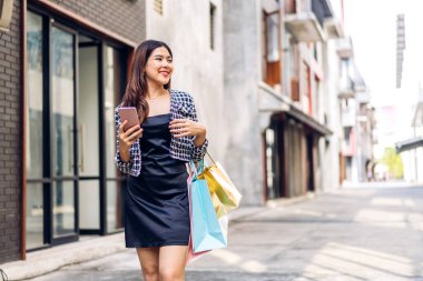 Gülümseyen güzel Asyalı moda mutlu kadın portresi rahatla ve alışveriş zamanının tadını çıkar yaz yürüyüşü ve alışveriş renkli bir çanta al bir şeyler almak için mağazada akıllı telefon kullan