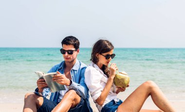 Romantik aşk genç mutlu gülümseme balayı seyahati çiftler mavi gökyüzü kumsalında kumlara oturup tropik plajlarda birlikte eğleniyorlar.