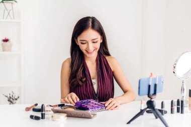 Neşeli, güzel bir kadının gülümsemesi taze, sağlıklı beyaz ten blogcusu kameranın önünde canlı yayın için video içeriği kaydediyor evde internet sosyal ağı için makyaj malzemesi ile konuşuyor.