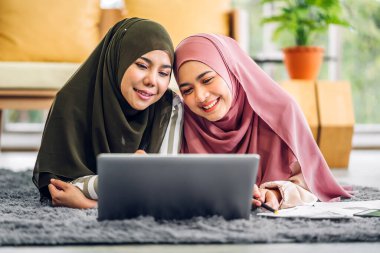 Gülümseyen mutlu Asyalı güzel Müslüman kadın dizüstü bilgisayarla rahatlıyor, çalışıyor ve analiz ediyor. Başlangıç projesi planı ve evdeki beyin fırtınası ile strateji tartışıyorlar.