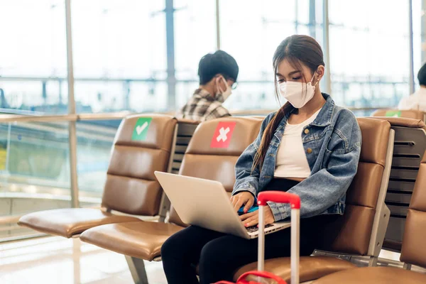 stock image Young woman in quarantine for coronavirus wearing surgical mask face protection during virus pandemic with social distancing use laptop with luggage wait flight travel at airport