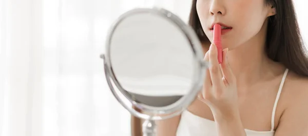 美しいアジアの女性の笑顔鏡を見て新鮮な健康的な肌と自宅で赤い口紅とスキンケア唇を適用楽しむ 顔の美しさと化粧品のコンセプト — ストック写真
