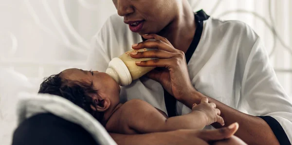 幸せな愛の家族の肖像画アフリカ系アメリカ人の母親は愛らしい小さなアフリカ系アメリカ人の赤ちゃんと遊んでいます 白い寝室でかわいい息子を赤ちゃんにミルクの母供給ボトル 黒家族の愛 — ストック写真