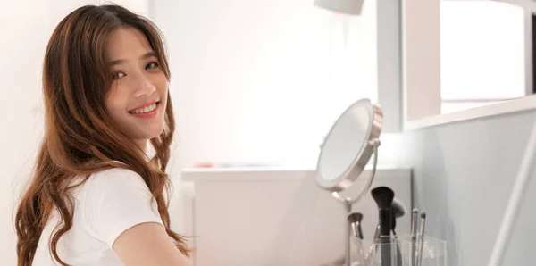 Smiling of young beautiful pretty asian woman clean fresh healthy white skin looking at mirror.asian girl touching on her face with hand and applying cream at home.spa and beauty concept