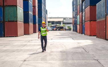 Kasklı profesyonel mühendis konteynır ustabaşı ayakta çalışıyor ve telsiz kullanıyor. Stokları yükleme için konteynıra koyuyor. Lojistik ulaşım ve iş sektörü ihracatı