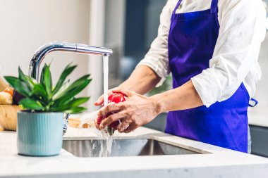 Erkek şefin portresi yemek pişirmek ve yemek hazırlamak taze sebze salatası suya sıçrıyor ve aşçı yemeği tezgahın üzerinde duruyor.