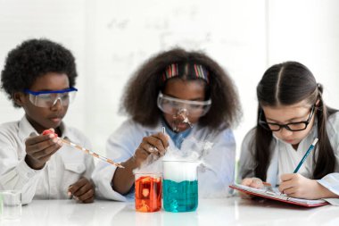 Bir grup genç öğrenci, kimya bilimi deneyi yaparak ve deney tüpünü el altında tutarak öğretmenle fen bilgisi öğreniyor. Eğitim.