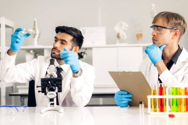 Profesyonel iki bilim adamı test tüpünde sıvı analiz ederken ve karıştırırken kimyasal bir deney yapıyor. Genç bilim adamı laboratuvarda cam üzerine kimyasal örnekler bırakıyor.