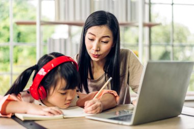 Anne ve Asyalı küçük kız öğreniyor ve online eğitim ile bilgisayar incelemesi yapıyor. Öğrenci evde eğitim bilgisini arıyor. Eğitim