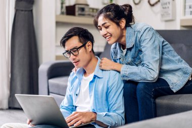 Genç Asyalı çift dizüstü bilgisayarla rahatlıyor ve video konferansında online sohbet ediyorlar. Yaratıcı iş çifti strateji analizi ve evde beyin fırtınası planlıyor.