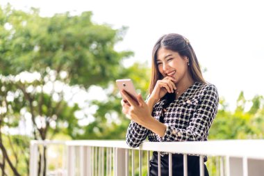 Gülümseyen mutlu Asyalı kadın portresi dijital akıllı telefon kullanarak rahatlıyor. Ekran daktilo mesajlarına bakan ve oyun oynayan Asyalı genç kız veya sosyal medya 