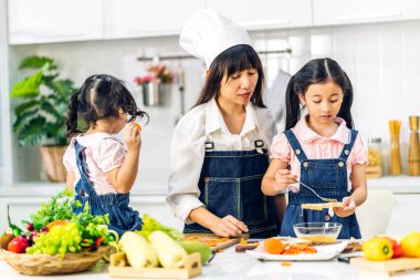 Mutlu bir aşk portresi. Asyalı bir anne ve küçük Asyalı bir kız çocuk. Mutfakta taze sebze salatası ve sandviç malzemesiyle birlikte sağlıklı yemekler pişirmeye yardım ediyorlar.
