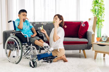 Özürlü çocuk sağlığı sorununa rehabilitasyon kliniğinde alıştırmalar yaparak yardım eden ve onunla oynayan Asyalı fizyoterapist portresi.