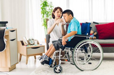 Mutlu aşk portresi. Asyalı anne oynuyor ve bakıcı tekerlekli sandalyede oturan engelli çocuğa bakıyor. Evde engelli bakımı konseptinde iyi vakit geçiriyor.
