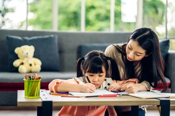 ポートレート幸せな愛アジアの家族の母親は 小さな娘アジアの女の子がテーブルの上で学び 研究を教えています お母さんとアジアの若い女の子は自宅でホームスクールで本や鉛筆作りの宿題で書く — ストック写真