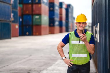 Kasklı profesyonel mühendis konteynır ustabaşı ayakta çalışıyor ve telsiz kullanıyor. Stokları yükleme için konteynıra koyuyor. Lojistik ulaşım ve iş sektörü ihracatı