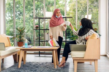 Gülümseyen mutlu Asyalı güzel Müslüman kadın dizüstü bilgisayarla rahatlıyor, çalışıyor ve analiz ediyor. Başlangıç projesi planı ve evdeki beyin fırtınası ile strateji tartışıyorlar.