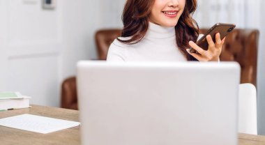 Genç gülümseyen mutlu Asyalı kadın evdeki yatak odasında dizüstü bilgisayar kullanarak rahatlıyor. Ev konseptinden çalışıp klavyede yazan genç yaratıcı kız.