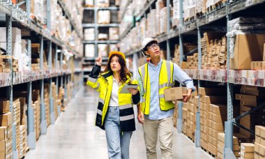 Asyalı iki mühendis ekibinin tablet üzerindeki sevkiyat emri. Raflardaki ürün ve malzemeleri kontrol et. Fabrika deposundaki ürün stokuyla birlikte.