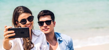 Romantik aşk genç mutlu gülümseme balayı çifti mavi gökyüzü kumsalındaki kumsalda tatil gezisinde tropikal sahilde birlikte eğleniyor ve dinleniyorlar.