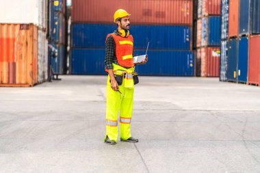 Kasklı profesyonel mühendis konteynır ustabaşı ayakta çalışıyor ve telsiz kullanıyor. Stokları yükleme için konteynıra koyuyor. Lojistik ulaşım ve iş sektörü ihracatı