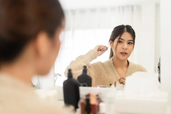 若い美しいアジアの女性の笑顔は鏡を見て新鮮な健康的な白い肌をきれいにします 手で彼女の顔に触れるアジアの女の子と自宅でクリームを適用します スパと美しさの概念 — ストック写真