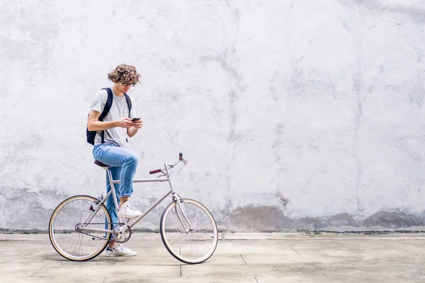 ストリートシティの道を自転車で通勤しながらスマートフォンを見ながらバックパック付きのカジュアルなヒップスターハンサムなビジネスマンの肖像画が仕事に行きます ビジネス旅行輸送自転車のコンセプト — ストック写真