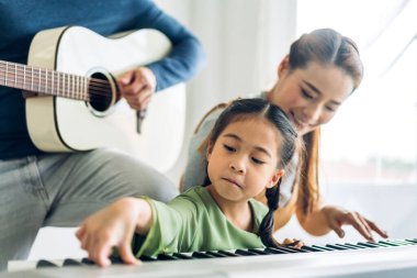 Mutlu aşk portresi Asyalı anne ve küçük Asyalı kız çocuk gülümseyip eğleniyorlar ve evde piyano dersi veriyorlar.