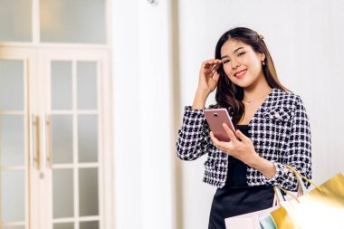 Gülümseyen güzel Asyalı moda mutlu kadın portresi rahatla ve alışveriş zamanının tadını çıkar yaz yürüyüşü ve alışveriş renkli bir çanta al bir şeyler almak için mağazada akıllı telefon kullan