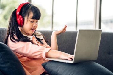 Öğrenci küçük kız öğreniyor ve dizüstü bilgisayara bakıyor ev ödevi yapıyor çevrimiçi eğitim sistemi ile bilgi öğreniyor. Evde öğretmenle çocuk video konferansı
