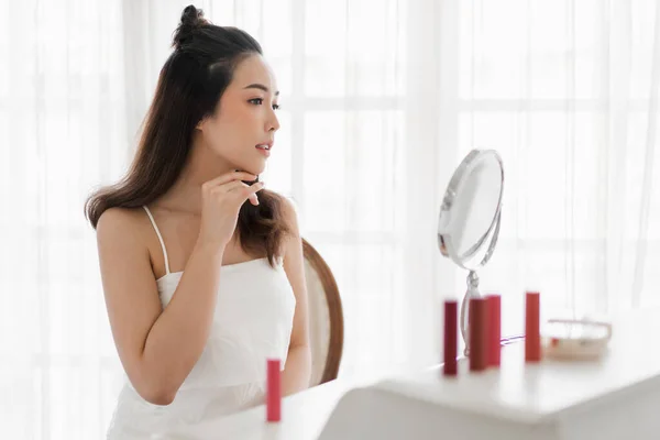 Smiling of young beautiful pretty asian woman clean fresh healthy white skin looking at mirror.asian girl touching on her face with hand and applying cream at home.spa and beauty concept