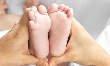 Sevgi dolu aile portresi. Anne sevimli küçük Asyalı bebekle oynuyor. Anne, tatlı oğluyla ayak teması kuruyor.