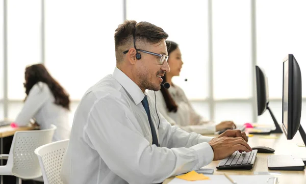 幸せなコールセンターの笑顔事業者のグループ顧客は コールセンターオフィスでデスクトップコンピュータ上のヘッドセットで作業し 話をチーム電話サービスをサポートする — ストック写真