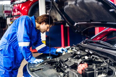 Üniformalı profesyonel araba teknisyeni araba motoru tamiri ve oto servisindeki araba kaputunun altındaki onarım onarım işlerini yapıyor. Otomobil servisi garajı