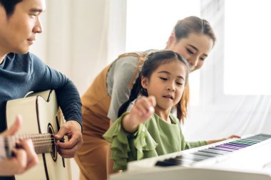Mutlu aşk portresi Asyalı anne ve küçük Asyalı kız çocuk gülümseyip eğleniyorlar ve evde piyano dersi veriyorlar.